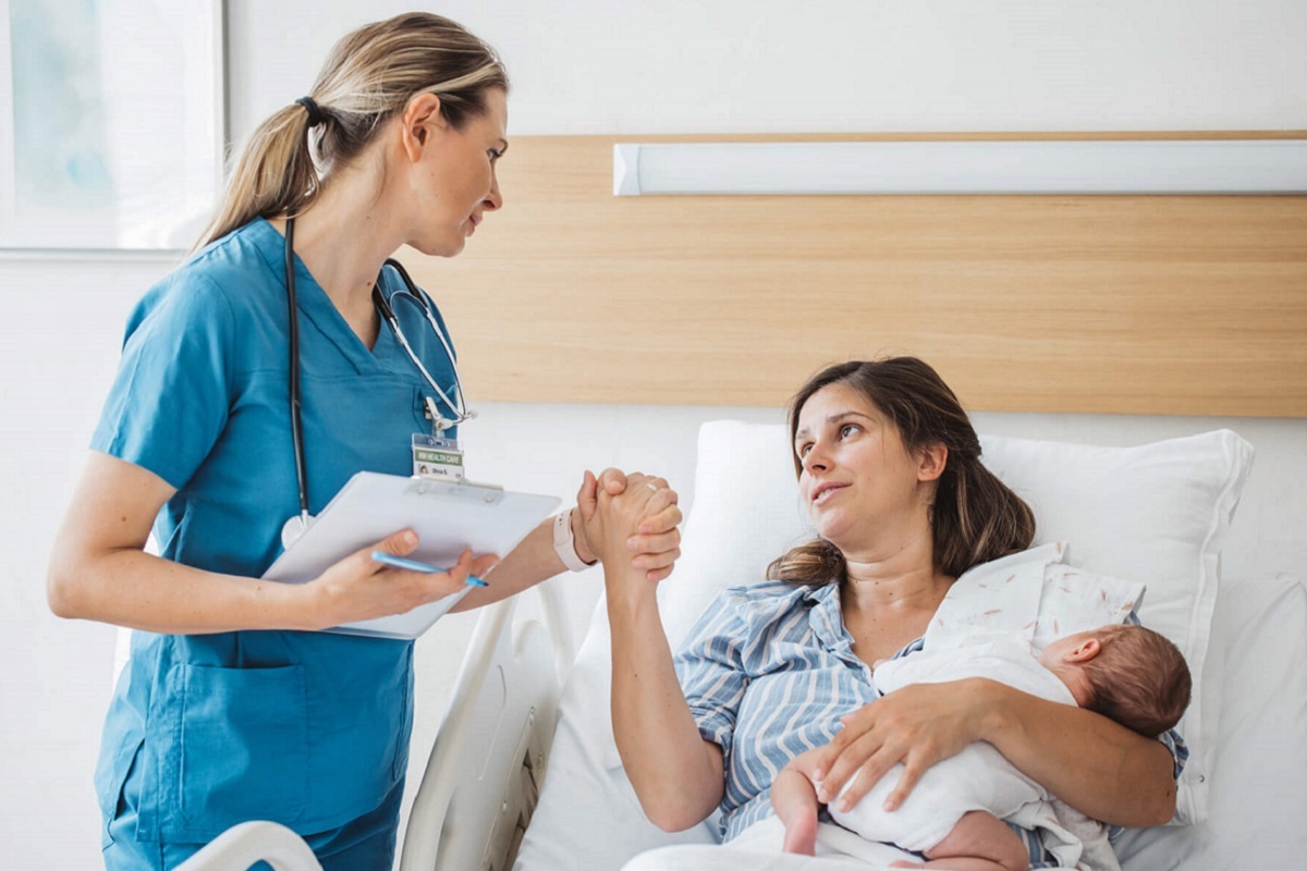 Nurse holding hand of new mom in hospital bed, showing their support of her new baby.