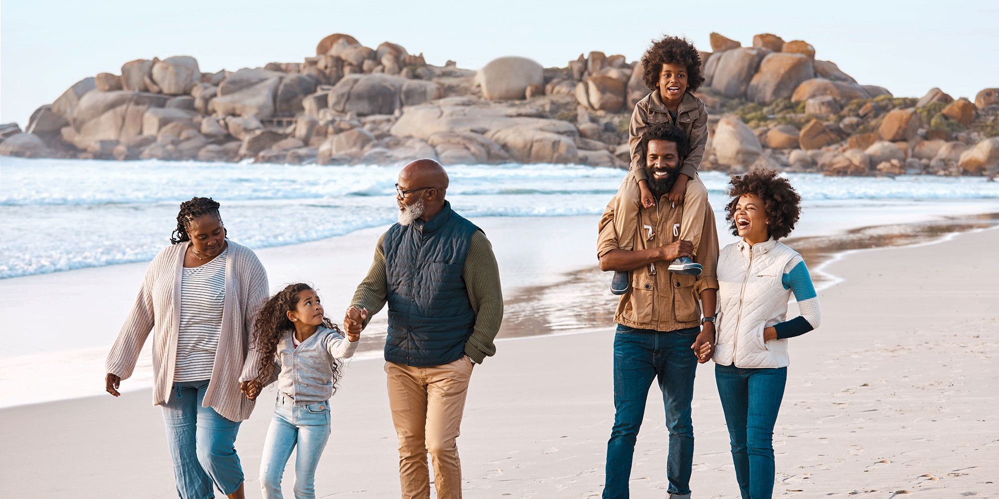 A family walks together on the beach. It's chilly, as it's overcast and they're all wearing warm clothes