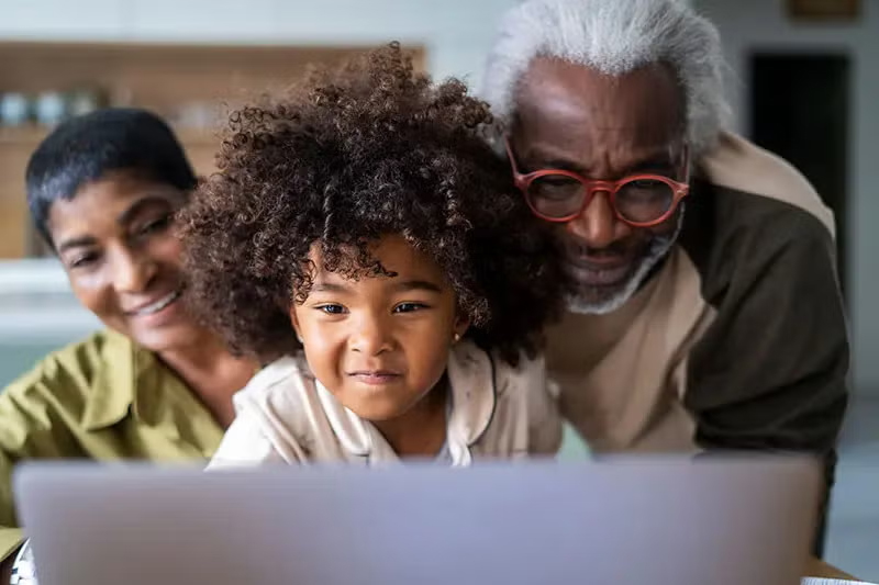 Grandparents and their young granddaugher huddle over a laptop together